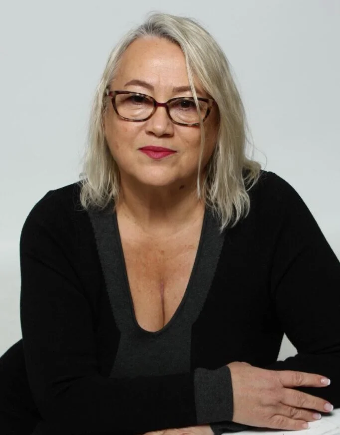 Woman with grey-blonde hair and tortoiseshell glasses in a black top, against a light grey background