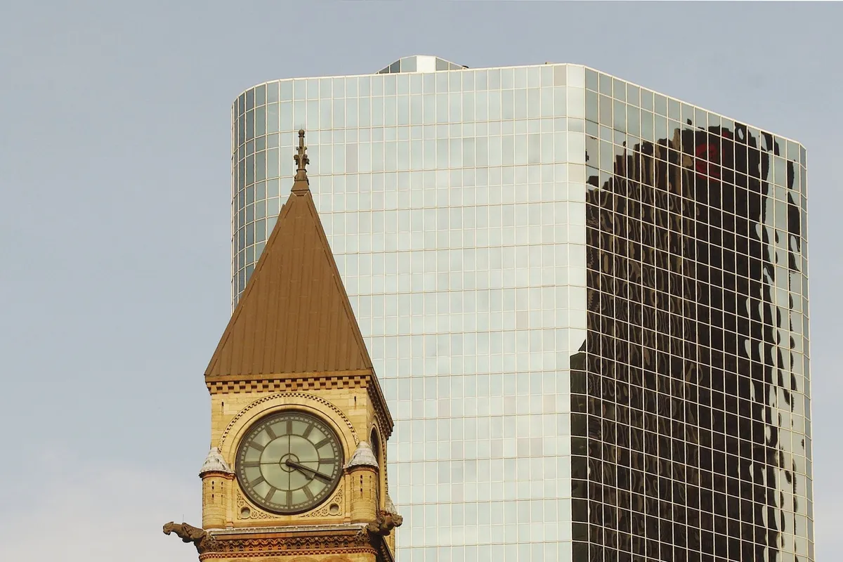 Clock tower of a historic stone building in front of a glass office tower