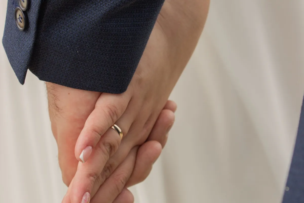 Two people holding hands, one wearing a wedding ring