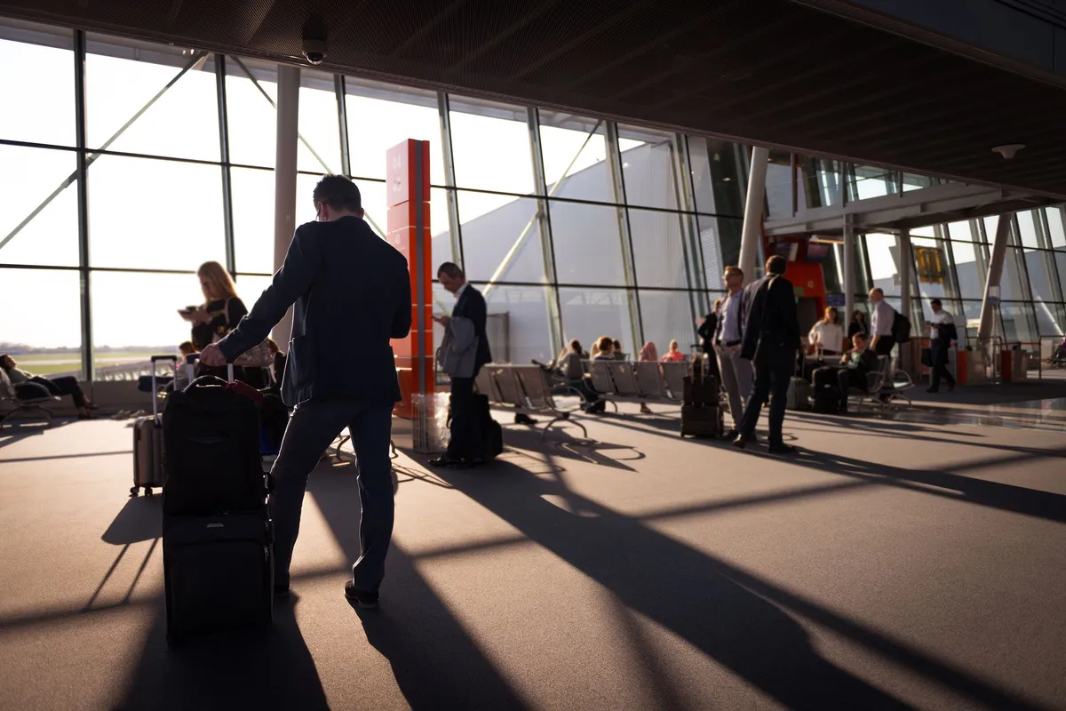 Travellers with luggage crossing a sunlit airport terminal