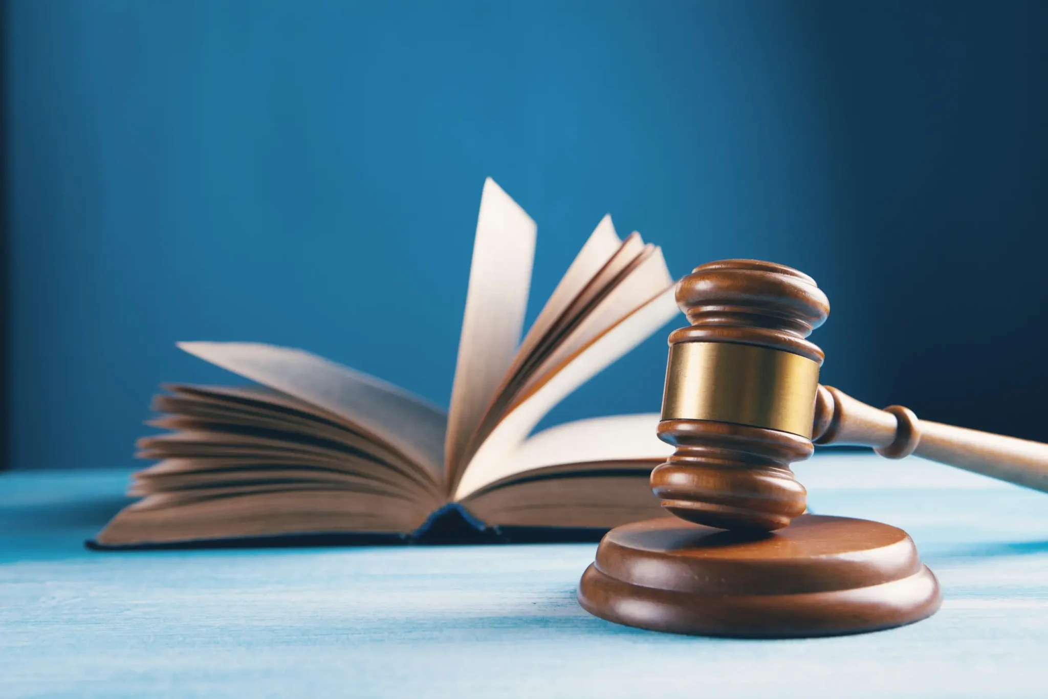 Wooden gavel with a brass band on its block in front of an open book with fanned pages, blue background